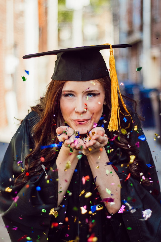 photo d'une femme avec un chapeau de ddiplomé qui souffle des confettis qu'elle tient dans les mains